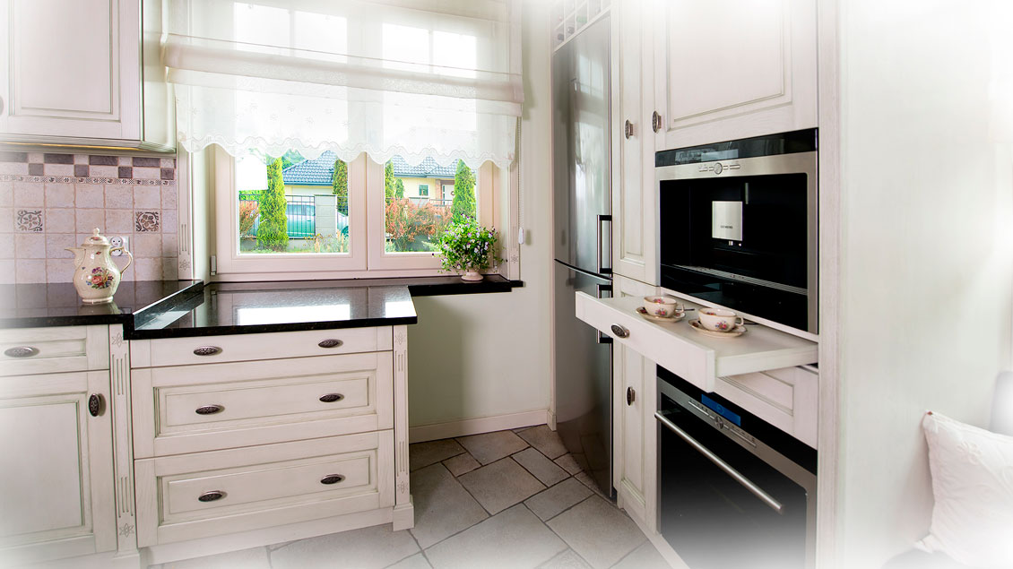 Ciemne blaty kuchenne i sprzęty AGD ładnie kontrastujące z białymi meblami kuchennymi i oknem.