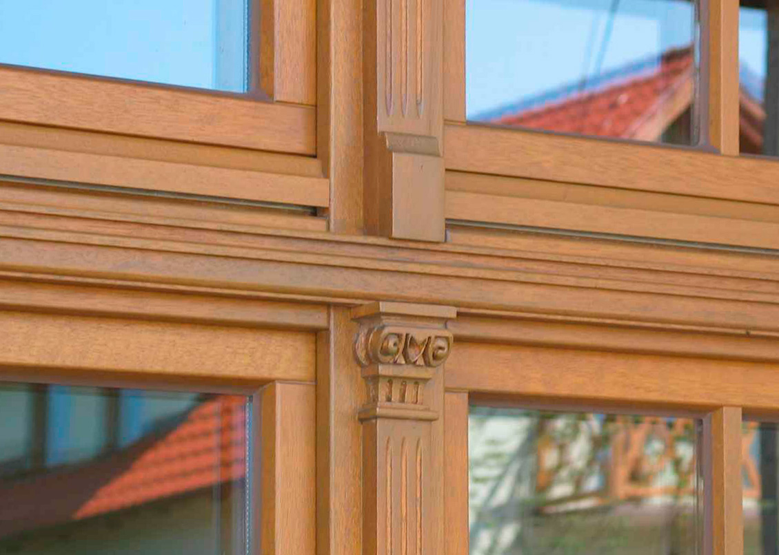 Drewniane okno na wymiar i drewniana zdobiona kolumienka z głowicą - fragment okna w kolorze naturalnym zdobiony pilastrem.