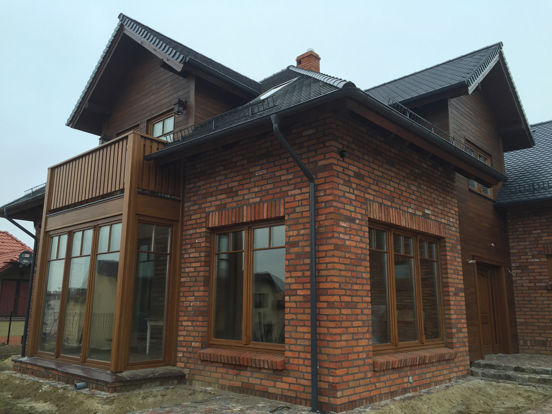 Drewniane okna na wymiar w kolorze brązowym, nowo budowany dom jednorodzinny, budowa jeszcze nieukończona.