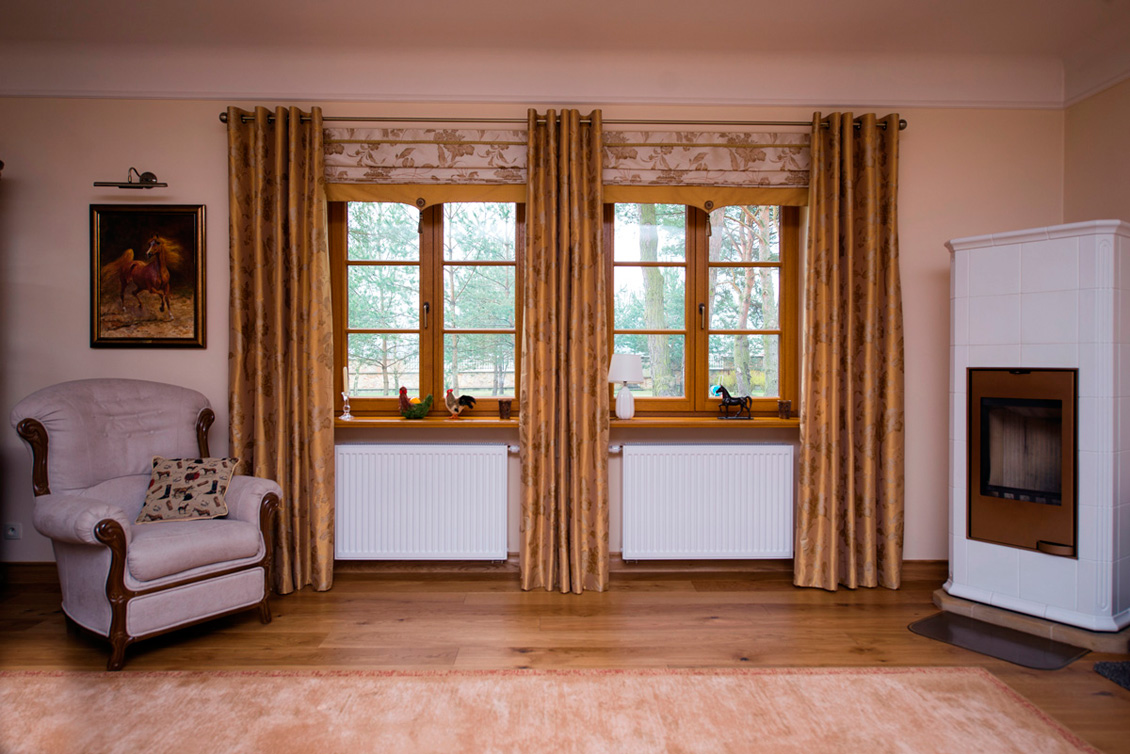 Drewniane okna na wymiar w kolorze naturalnym w eleganckim salonie z fotelem, kominkiem i obrazem.