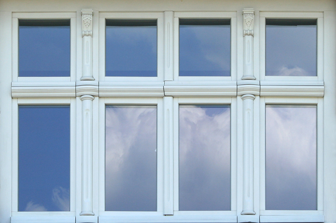 Białe drewniane okno na wymiar, widok z zewnątrz, okno zdobione kolumienkami.
